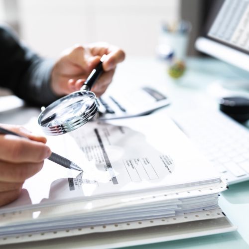 Audit And Fraud Investigation. Auditor Using Magnifying Glass On Document